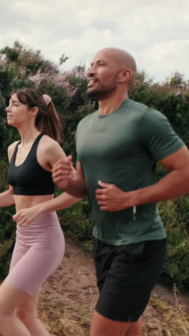 Vertical video, Side view of running multiethnic woman and man enjoy their summer morning outdoors workout. Team sports. Couple goals and motivation. Happy fit people are cheerfully doing sports