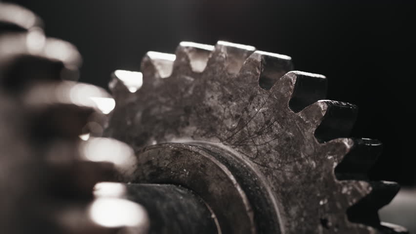Two rotating metal gears. Gear movement. A moving part of an engine or transmission. Part of a factory conveyor.