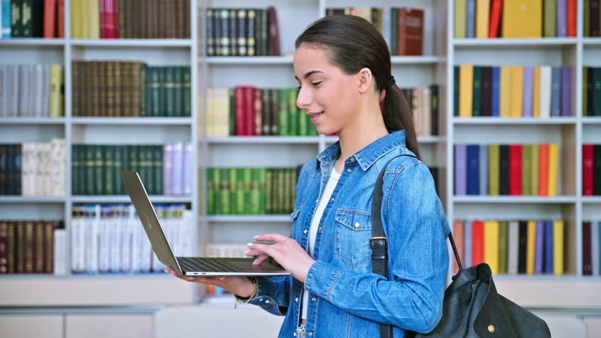 Teenage girl student using laptop, inside high school building, in library