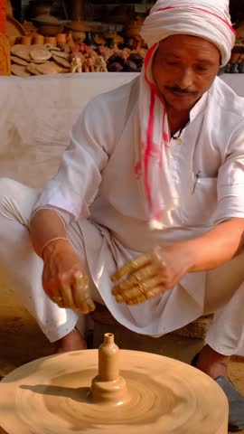 Indian potter at work: throwing the potter's wheel and shaping ceramic vessel and clay ware: pot, jar in pottery workshop. Experienced master. Handwork craft from Shilpagram, Udaipur, Rajasthan, India