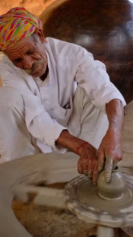 Skilled professional potter throwing the potter's wheel and shaping traditional ceramic vessel and clay ware: pot, jar in pottery workshop. Handwork craft from Shilpagram, Udaipur, Rajasthan, India