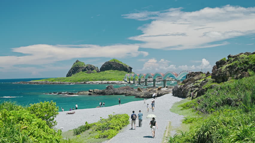 Sanxiantai Arch Bridge in Taitung, Taiwan, under a sunny sky with light clouds, a few people enjoying the clear day.