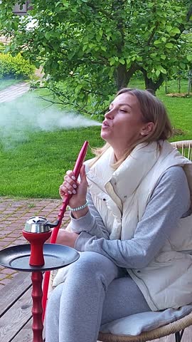 Woman smokes hookah on in backyard. Outdoor recreation with friends Vertical video. Taken from hand. High quality 4k footage