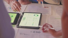 A team of business professionals intensely reviews ESG performance metrics on a tablet, focusing on environmental and sustainability data during a corporate strategy meeting. - Powered by Shutterstock - Get 15% off with code: PIKWIZARD15