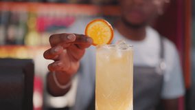 Bartender puts orange slice and straw into cocktail closeup. African American man decorates citrus beverage in nightclub. Refreshing party drink - Powered by Shutterstock - Get 15% off with code: PIKWIZARD15