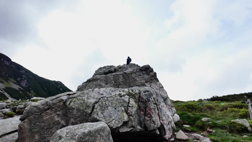 A black raven, against the background sky, flies away from a rock.