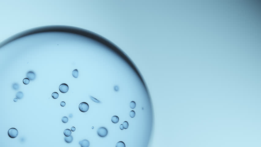 Macro shot of drops of pure fresh melt mountain water with tiny air bubbles, small droplets separate from the large water sphere and fly away on a bright light blue background