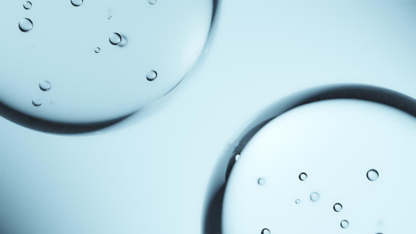Macro shot of drops of pure fresh melt mountain water with tiny air bubbles, the drops are moving and merging into a large water sphere on a bright light blue background