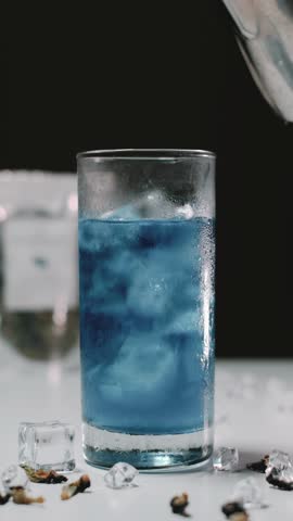 The process of making a Butterfly Pea Milk Tea in a glass with ice. Portrait or vertical footage. Bokeh background.