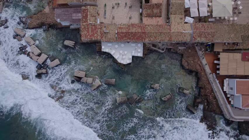 Aerial Top down waves crashing into a restaurant deck, Marzamemi, Sicily
