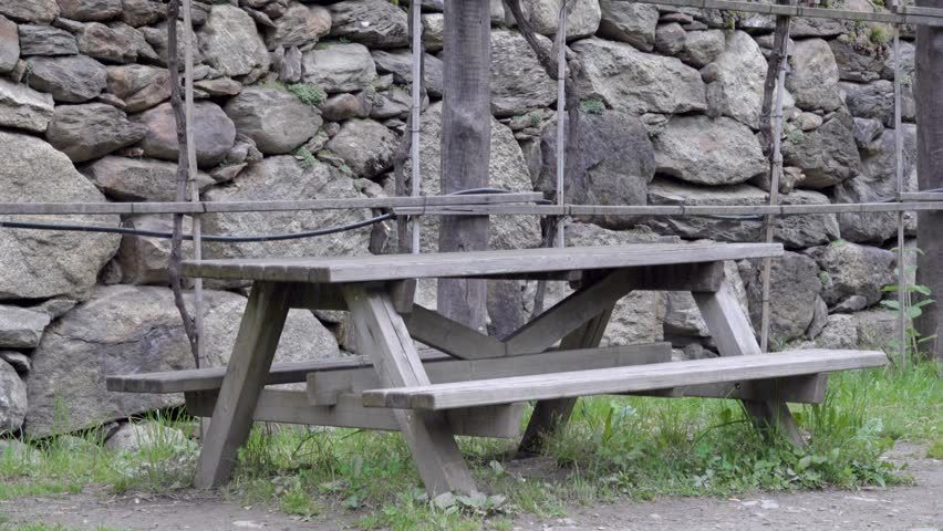 Wooden outdoor picnic table with two integrated benches in front of a stone wall.