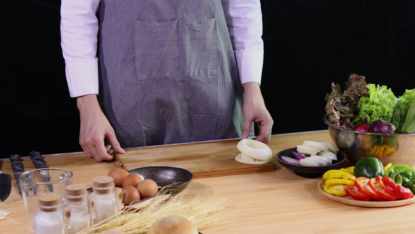 Young Chef holding and knocking boiled egg and preparing it on wooden cutting board with fresh vegetables, eggs, and spices on kitchen counter