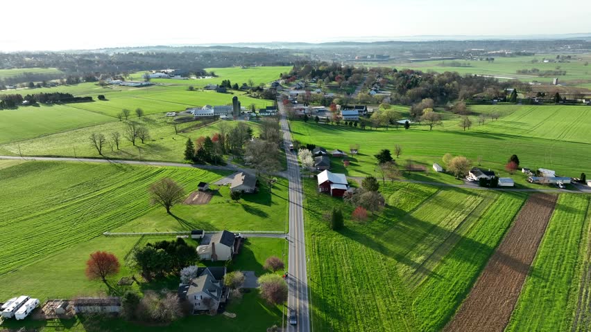 Driving cars on rural intersection in countryside of american town. SUnny day in spring season. Green farm fields and farm houses. Aerial birds eye forward shot.