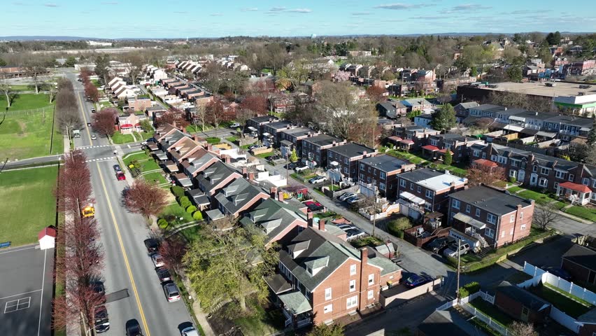 Row of houses in small american suburbia during sunny day. Spring season with traffic on main street. Middle Class Residential area in USA. Aerial panning wide shot.