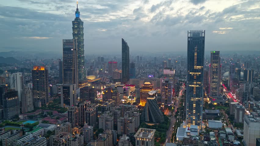 Aerial hyperlapse at moody dusk above Downtown Taipei, the vibrant capital city of Taiwan, with 101 Tower standing amid skyscrpers in XinYi Commercial District and city lights dazzling in the night