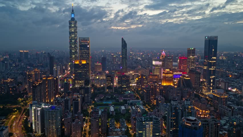 Aerial hyperlapse at moody dusk above Downtown Taipei, the vibrant capital city of Taiwan, with 101 Tower standing amid skyscrpers in XinYi Commercial District and city lights dazzling in the night