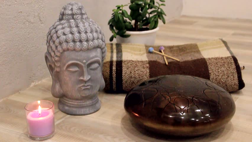 Burning candle next to Buddha's head and Hapi Drum in video