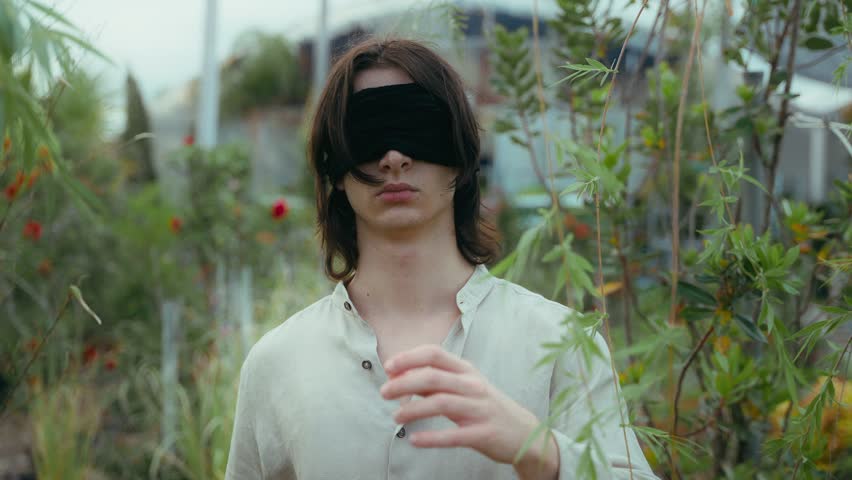 cinematic middle shot of young man walking in plant nursery with blindfolded eyes