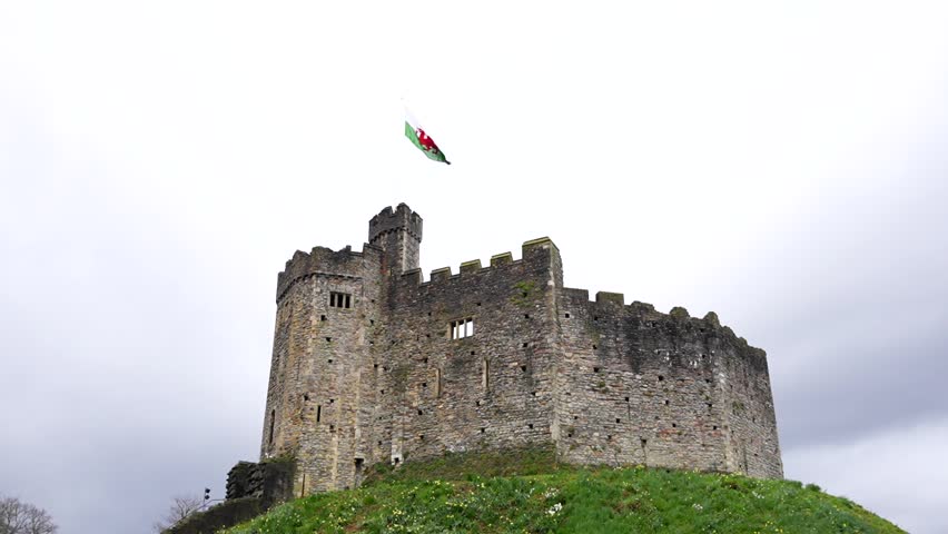 Norman Fortress of Cardiff Castle, Welsh flag with dragon waving against wind. Slomo tilt up