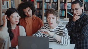 Group of young multi-ethnic students standing around girl explaining them project on laptop monitor in college library - Powered by Shutterstock - Get 15% off with code: PIKWIZARD15