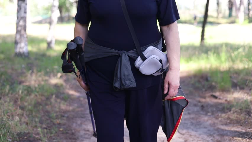 Smiling senior women in sport clothes walking outside after Nordic walking holding the trekking poles. Elderly female after training. Aging youthfully.