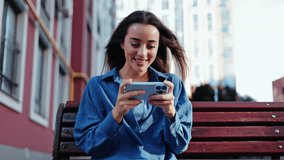 A happy young woman is fully engrossed in playing a mobile game outdoors, her joyful reactions showing the excitement of the competition. - Powered by Shutterstock - Get 15% off with code: PIKWIZARD15