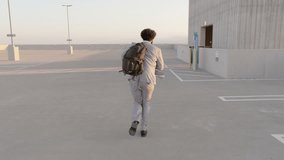 In a rooftop parking lot, a young businessman in a suit rushes to the elevator with a backpack, against a sunset city skyline. It depicts a modern urban professionals daily hustle - Powered by Shutterstock - Get 15% off with code: PIKWIZARD15