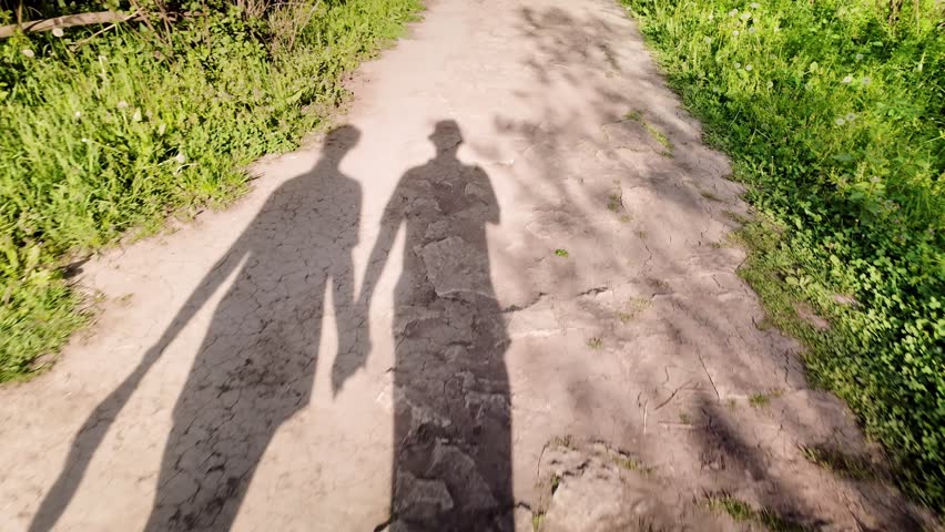 Long silhouette shadows of couple walking along nature trail hand in hand