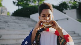 A cheerful boy is enjoying a burger outdoors wrapped in an American flag, reflecting patriotism and freedom while celebrating youth and simple pleasures under the sunny sky - Powered by Shutterstock - Get 15% off with code: PIKWIZARD15