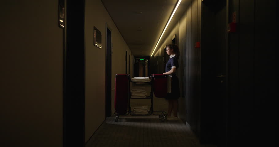 Young Female Housekeeper In Hotel Corridor, Zooming Shot, Portrait From Side During Daily Cleaning