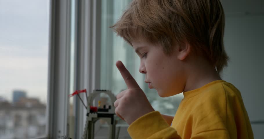 Kid Boy Plays With Toy Constructor Building on Windowsill Near Window. City Apartment Building 4K 10-bit