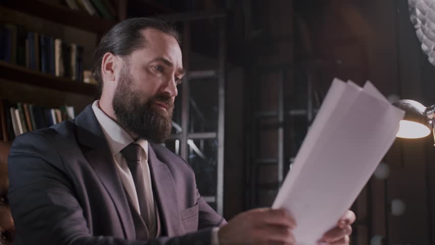 A businessman is carefully examining documents on his office desk with focus and concentration