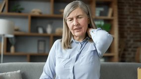 Tired senior female suffering from neck pain while sitting on the sofa in the living room at home. Upset elderly retired woman massages and rubs sore muscles with her hands, stretches. Close up - Powered by Shutterstock - Get 15% off with code: PIKWIZARD15