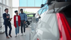 Handsome car dealer with tablet device walking with couple and looking at cars. Manager talking about all functions of family car. Buyers looking through window into car with interest. - Powered by Shutterstock - Get 15% off with code: PIKWIZARD15
