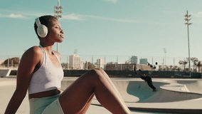 Close-up of young athletic woman sits in a skatepark on a hot summer day, with skateboarders performing tricks in the background - Powered by Shutterstock - Get 15% off with code: PIKWIZARD15