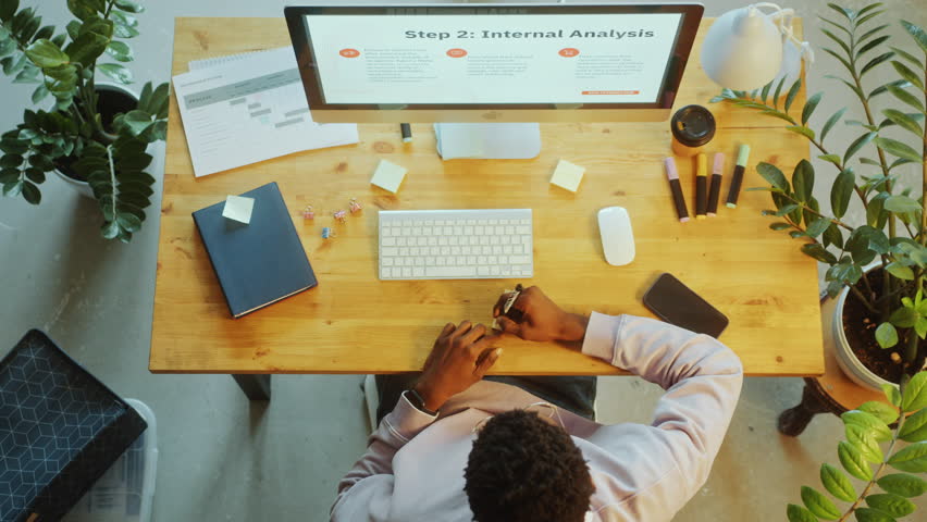 Black businessman using computer, writing sticky notes and attaching them to desk during workday in the ofice. Time lapse, directly above view