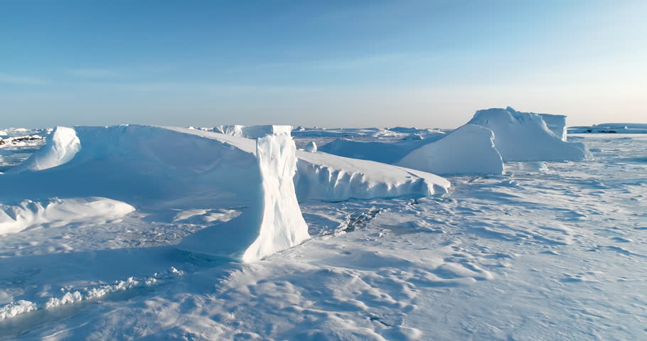 Frozen polar ocean landscape in Antarctica. Icebergs and glaciers stuck in snow covered ice water. Cold winter scene. Arctic environment preserve of ice. Blue sky sunny day. Aerial panorama zoom out
