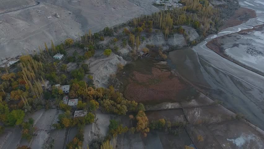 Aerial view of Indus River surrounded by trees, rocks, and hills in autumn, Khaplu, Gilgit-Baltistan, Pakistan.