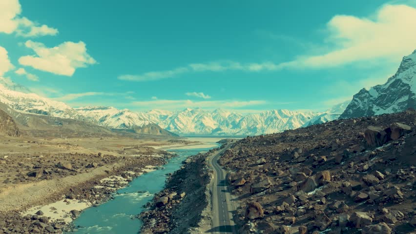 Drone is flying slowly over a river in Skardu with a view of a high mountain range covered in snow
