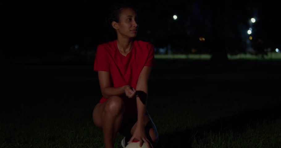 At night, a young girl in a bikini has a football in her hand.
