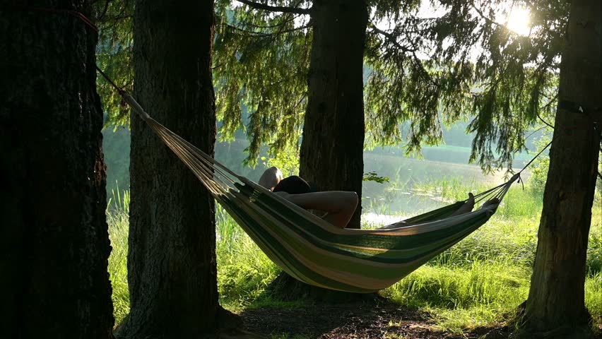 A man relaxes lying in a hammock, in a beautiful landscape, on the shore of the lake, among the trees. In camping, in nature. - Powered by Shutterstock - Get 15% off with code: PIKWIZARD15