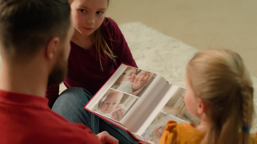 Caucasian parent father and children kids laughing having fun together enjoy evening weekend happy dad daughters babies siblings little girls hold book with funny photos watching family photo album