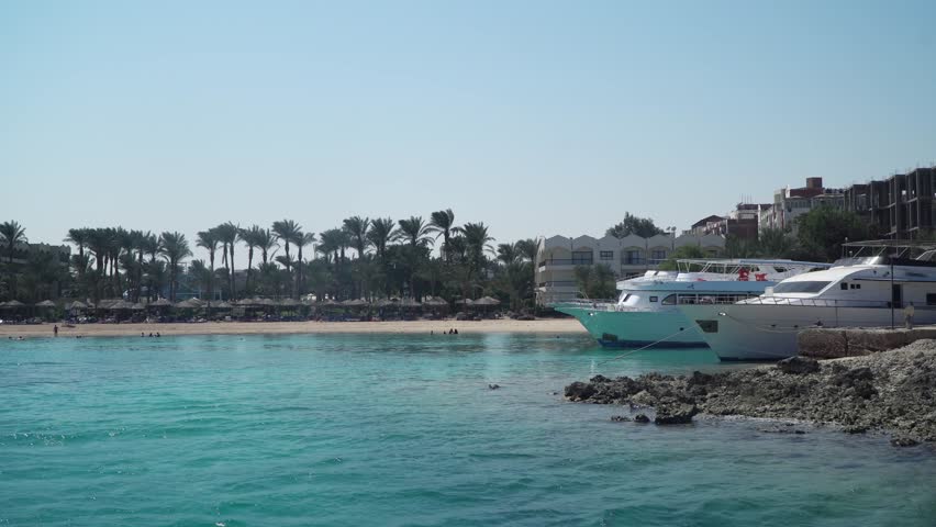 Tropical establishing shot of beautiful blue ocean laguna with a yacht boats docked on the shore and palm trees at background. Scene is peaceful and relaxing