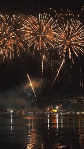Bright fireworks exploding with colorful lights over sea shore and small mediterranean town. Vertical video
