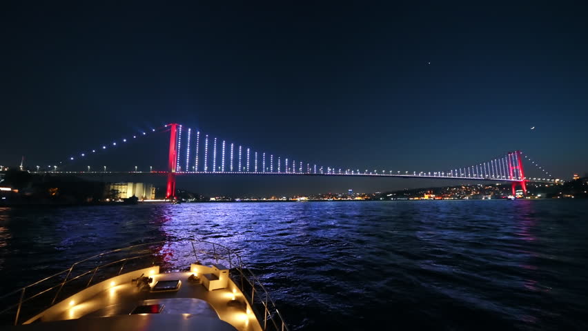 View of Bosphorus Bridge at night in Istanbul, Turkey. View from a floating ship, illumination, moving on the bridge cars