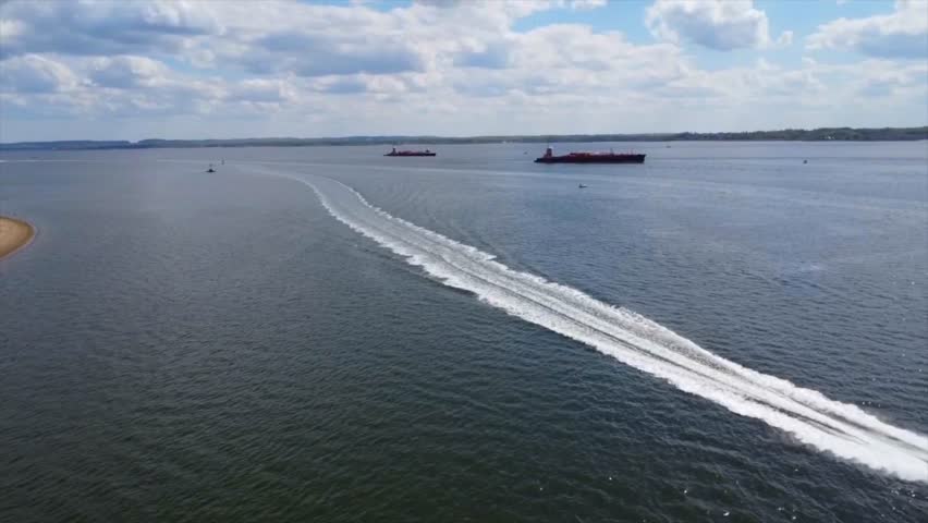 A ladscape scene of sea with speed boats and green hills with gray cloudy sky