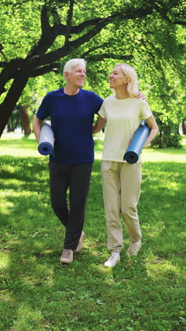 Senior couple walks together in park, carrying yoga mats, enjoying fresh air and each other's company. Concept of active lifestyle, healthy aging and companionship in golden years