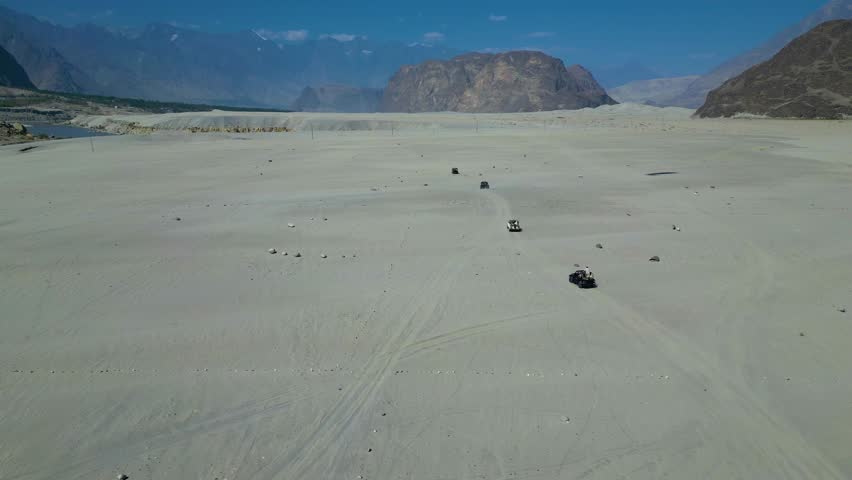 High angle drone shot of mountain terrain vehicles driving on Sarfaranga Cold Desert in Skardu valley, Pakistan.