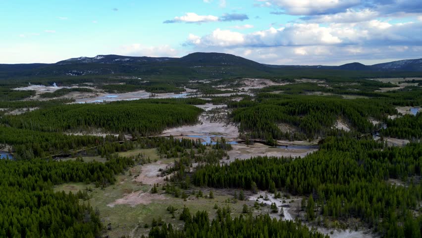 An aerial view of the Firehole River flowing through vast lands with dense green trees in Yellowstone National Park, Wyoming, United States