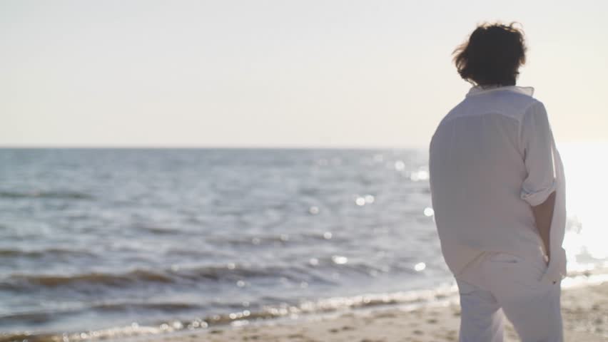 A stylish man in white beachwear and sunglasses stands by the sea, exuding confidence and elegance. Perfect for fashion, travel, and lifestyle promotions showcasing beach style and luxury. 